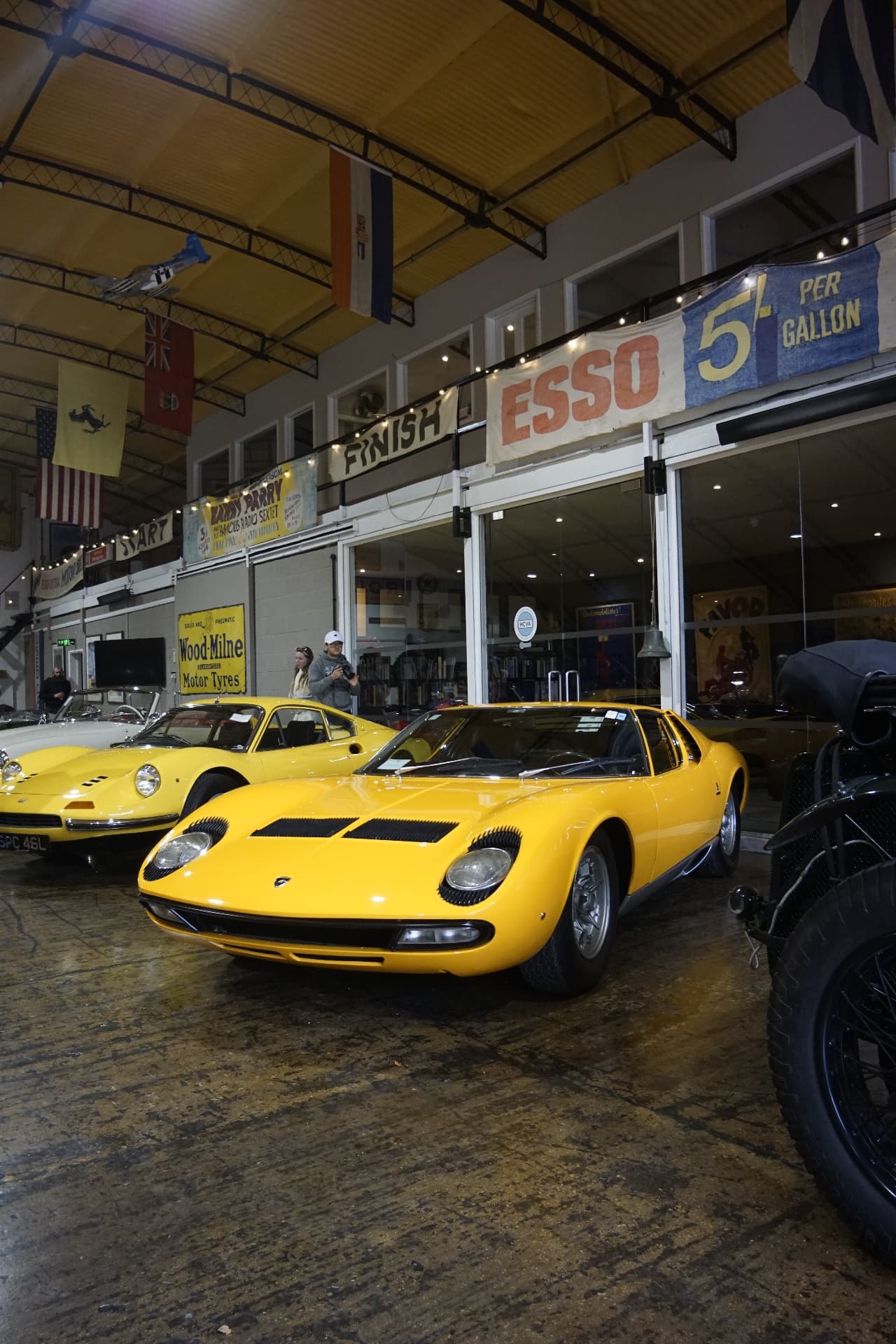 Yellow Lamborghini Miura beneath vintage motoring signs in the showroom