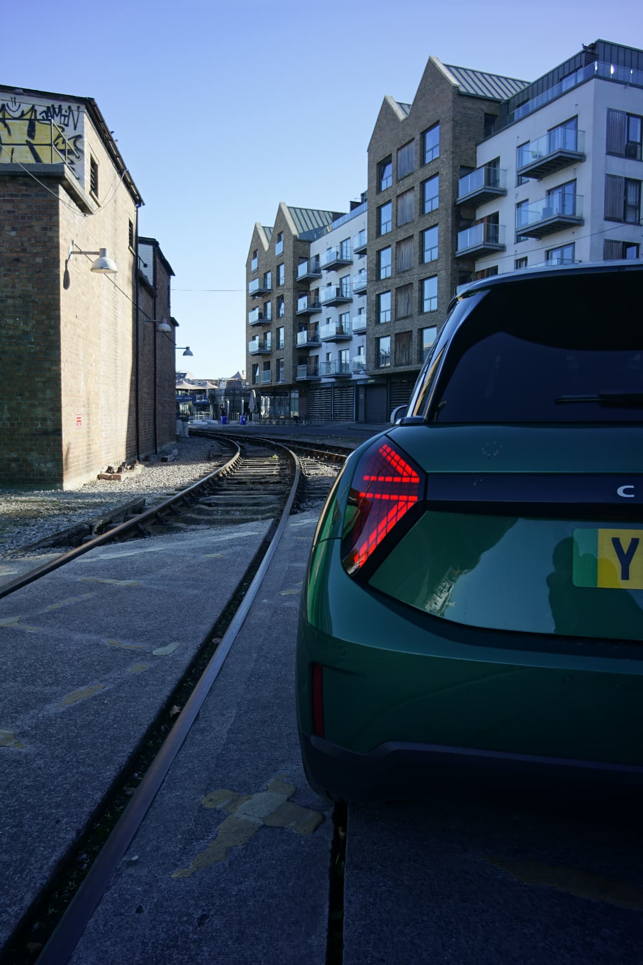 Illuminated triangular Union Jack rear light on the MINI Cooper E beside dockside railway tracks