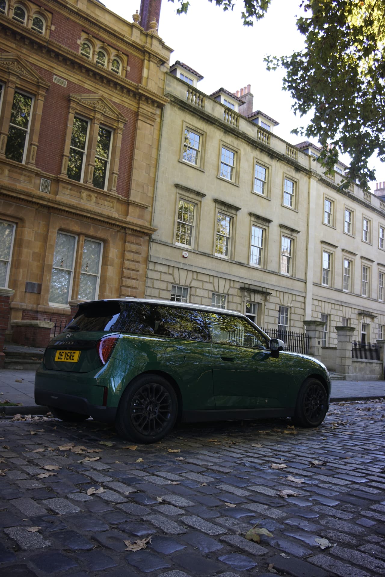 Rear three-quarter view of the green MINI Cooper E on cobbles beneath historic buildings